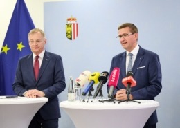 2 Personen hinter Rednerpulten mit Mikrophonen.