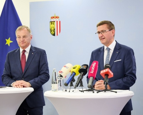 2 Personen hinter Rednerpulten mit Mikrophonen.