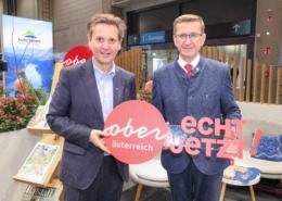 Zwei Herren im Anzug halten ein Plakat. Auf dem Plakat steht "Oberösterreich: echt jetzt"