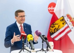 ein Mann steht auf einem Tisch mit vielen Mikrofonen und redet.