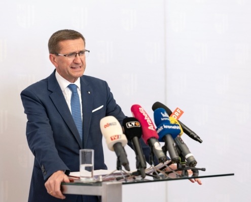 Ein Mann steht an einem Pult mit vielen Mikrofonen und spricht.