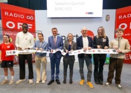 Sieben Menschen stehen vor der Kamera und lächeln. Sie halten eine Papierschlange in der Hand.