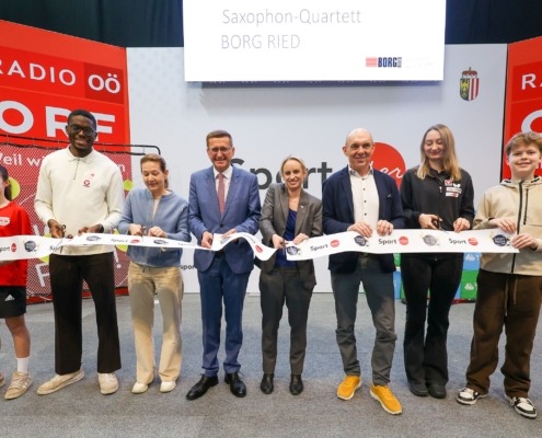 Sieben Menschen stehen vor der Kamera und lächeln. Sie halten eine Papierschlange in der Hand.