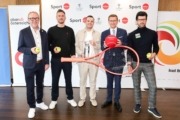 Fünf Herren stehen nebeneinander und lächend in die Kamera. jeder hält einen Tennisball und gemeinsam halten sie einen sehr großen Tennisschläger.