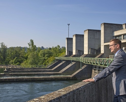 Ein Herr steht vor einer Wasserkraftanlage und blickt in die Natur.