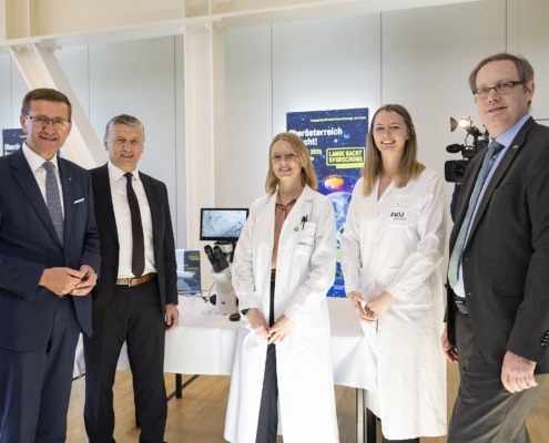 Fünf Personen stehen vor einem Tisch und lächeln in die Kamera. Zwei Damen haben einen weißen Kittel an.