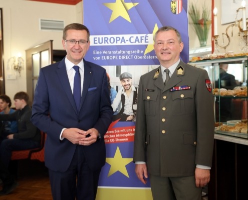 Zwei Herren stehen vor einem Poster und lächeln in die Kamera