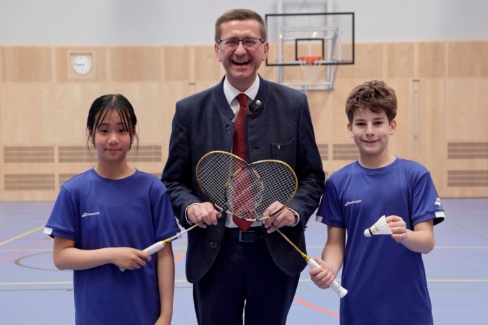 © Land OÖ Landesrat Achleitner mit zwei Kindern, die Badminton-Schläger halten.