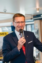 Ein Mann im Anzug spricht mit einem Mikrofon in der Hand und lächelt.