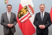 Zwei Herren stehen im Anzug vor einer Wand und lächeln in die Kamera