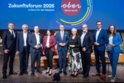 mehrere Personen stehen vor einer Oberösterreich Präsentation und lächeln in die Kamera.