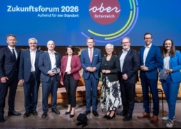 mehrere Personen stehen vor einer Oberösterreich Präsentation und lächeln in die Kamera.