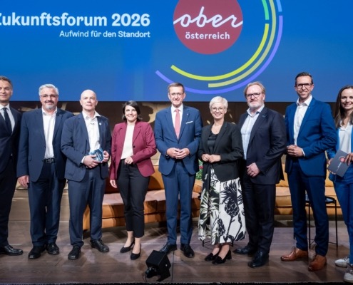 mehrere Personen stehen vor einer Oberösterreich Präsentation und lächeln in die Kamera.