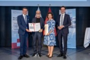 Auszeichnung mit dem FH OÖ-Ehrenring - v.l.: Wirtschafts- und Forschungs-Landesrat Markus Achleitner, Univ.-Prof. Dr. Gustav Pomberger, MMag.a Isolde Perndl, Kaufmännische Geschäftsführerin FH OÖ, und Dr. Michael Rabl, Hochschulpräsident FH OÖ. Vier Menschen stehen auf einer Bühne und halten ein Zeugnis in der Hand.