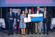 Teufelberger-Master-Thesis-Award an DI Manuel Schachinger vergeben – v.l.: Wirtschafts- und Forschungs-Landesrat Markus Achleitner, Studiengangsleiter Dr. Daniel Heim, MMag.a Isolde Perndl, Kaufmännische Geschäftsführerin FH OÖ, DI Manuel Schachinger, Mag. Florian Teufelberger, CEO Teufelberger AG, Dr. Michael Rabl, Hochschulpräsident FH OÖ. Viele Meschen stehen auf einer Bühne und halten ein Plakat in der Hand.