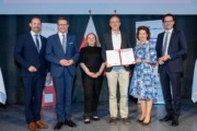 Dr. rer. pol. Valentin Schmidt wurde der Titel FH-Professor verliehen - v.l.: Dr. Andreas Auinger, Dekan der FH OÖ Campus Steyr, Wirtschafts- und Forschungs-Landesrat Markus Achleitner, Dipl.oec.troph Claudia Probst für das Kollegium der FH OÖ, Dr. rer. pol. Valentin Schmidt, MMag.a Isolde Perndl, Kaufmännische Geschäftsführerin FH OÖ, und Dr. Michael Rabl, Hochschulpräsident FH OÖ. Viele Menschen stehen auf einer Bühne und halten ein Zeugnis in der Hand. Hinter ihnen sind Flaggen.