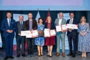 Mit dem Forscher/innenpreis wurden Dr. Johannes Preiner, Dr. Karin Nachbagauer und Dr. Wolfgang Schildorfer geehrt – v.l.: Wirtschafts- und Forschungs-Landesrat Markus Achleitner, Dr. Johann Kastner, Vizepräsident für F&E, Dr. Johannes Preiner, MMag.a. Isolde Perndl, Kaufmännische Geschäftsführerin FH OÖ, Dr. Karin Nachbagauer, Dr. Wolfgang Schildorfer, Dr. Michael Rabl, Hochschulpräsident FH OÖ, Sandra Mühlböck, Moderation. Viele Meschen stehen auf einer Bühne und halten Plakate in der Hand.