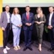 Fünf Personen stehen auf einer Bühne. Sie sind elegant gekleidet und lächeln in die Kamera.