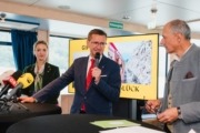 Ein Herr steht vor einem Tisch und spricht mit einem Mikrofon in der Hand.