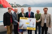 Sieben Personen stehen auf einem Boot während sie ein Plakat in der Hand halten und in die Kamera lächeln.