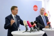 Zwei Herren stehen an einem Tisch mit Mikrofonen und reden.