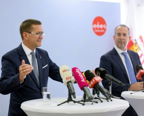 Zwei Herren stehen an einem Tisch mit Mikrofonen und reden.