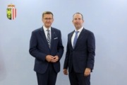 Zwei Herren stehen elegant gekleidet von einer Wand und lächeln in die Kamera.