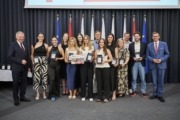 Landeshauptmann Mag. Thomas Stelzer und Wirtschafts- und Sport-Landesrat Markus Achleitner gratulieren den Linz AG Steelvolleys. Viele Personen stehen vor vielen Flaggen und halten Auszeichnungen in der Hand.