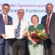 Vier Personen stehen vor einer Sport-Wand und lächeln mit Auszeichnungen in der Hand in die Kamera.