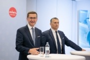 Zwei Herren im Anzug stehen vor Hochtischen.