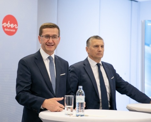 Zwei Herren im Anzug stehen vor Hochtischen.