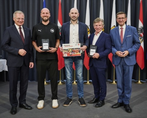 Fünf Männer stehen vor vielen Flaggen und lächeln in die Kamera.