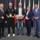 Fünf Männer stehen vor vielen Flaggen und lächeln in die Kamera.