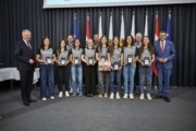Landeshauptmann Mag. Thomas Stelzer und Wirtschafts- und Sport-Landesrat Markus Achleitner gratulieren der Union Compact Freistadt. Viele Personen aus einer Sportmannschaft stehen vor vielen Flaggen und lächeln in die Kamera.