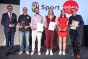 Auszeichnung mit dem Landes-Sportehrenzeichen in Gold: Wirtschafts- und Sport-Landesrat Markus Achleitner ehrte zahlreiche Sport-Persönlichkeiten, darunter (v.l.) Paragleiter Manfred Ruhmer, Badminton-Ass Wolfgang Gnedt, Michelle Schnepfleitner (ASVÖ SV Rosenau-Edlbach), Silvia Anzinger (OÖ-Leichtathletikverband) und Robert Machtlinger (Schärdinger Flieger-Union). Sechs Personen stehen mit Auszeichnungen in der Hand vor einer Sport-Wand.