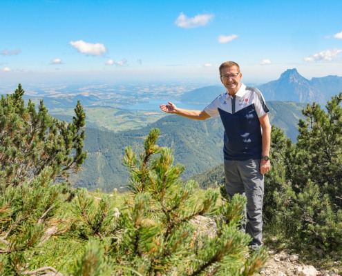 Ein Mann steht in der Natur und zeigt in die Berge im Hintergrund.