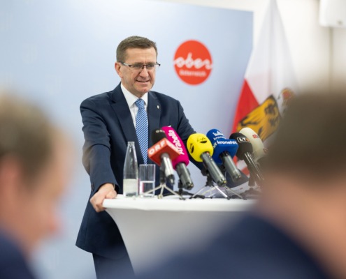 Ein Mann steht an einem Tisch mit Mikrofonen und spricht ins Publikum.