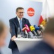 Ein Mann steht an einem Tisch mit Mikrofonen und spricht ins Publikum.