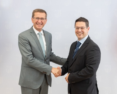 Zwei Herren stehen vor einer Wand und geben sich die Hand.