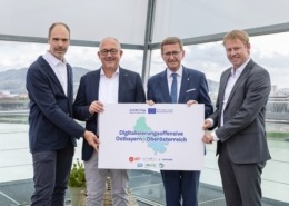 Vier Personen stehen vor der Kamera und halten ein Plakat in der Hand.