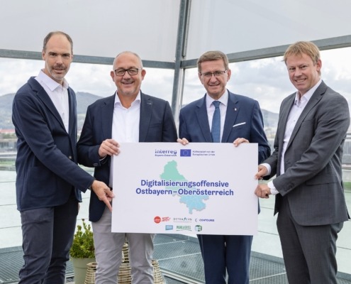 Vier Personen stehen vor der Kamera und halten ein Plakat in der Hand.