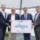 Vier Personen stehen vor der Kamera und halten ein Plakat in der Hand.