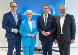 Vier Personen stehen vor einer blauen Wand uns lächeln in die Kamera.