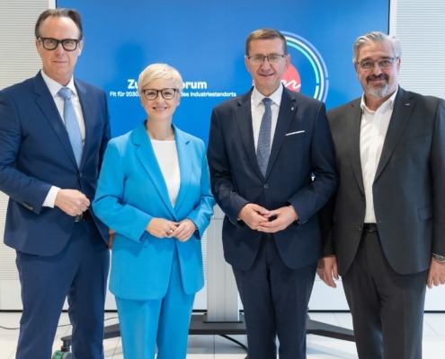 Vier Personen stehen vor einer blauen Wand uns lächeln in die Kamera.