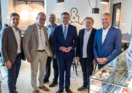 Sechs Herren stehen elegant gekleidet vor der Kamera und lächeln.