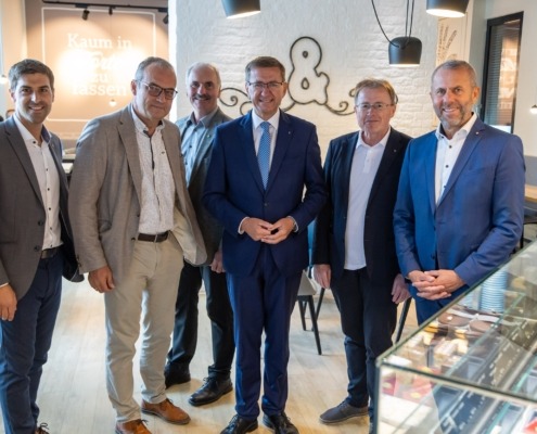 Sechs Herren stehen elegant gekleidet vor der Kamera und lächeln.