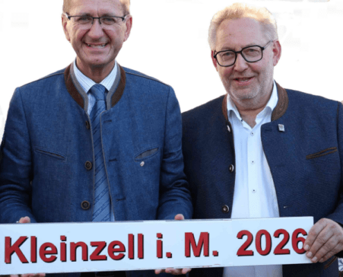 Zwei Herren stehen in der Natur und halten ein Schild in der Hand.