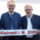 Zwei Herren stehen in der Natur und halten ein Schild in der Hand.