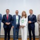 Eine Gruppe von sechs Personen steht gemeinsam für ein Foto vor einer hellen Wand. Die Personen tragen Businesskleidung und lächeln in die Kamera.