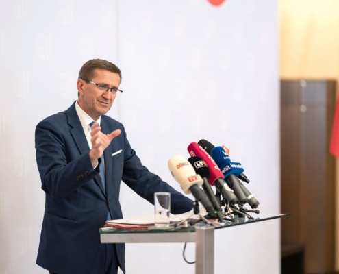 Wirtschafts-Landesrat Markus Achleitner vor einem Tisch mit vielen Mikrofonen von diversen Nachrichtensender.